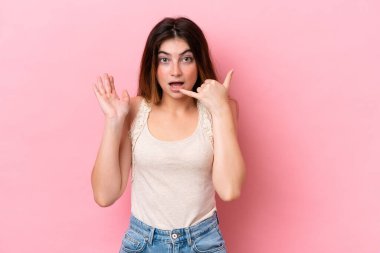 Pembe arka planda izole edilmiş genç beyaz bir kadın telefon jesti yapıyor.