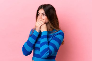 Pembe arka planda izole edilmiş genç beyaz kadın ağzını kapatıyor ve yan tarafa bakıyor.