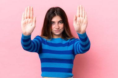 Pembe arka planda izole edilmiş genç beyaz kadın dur hareketi yapıyor ve hayal kırıklığına uğruyor.