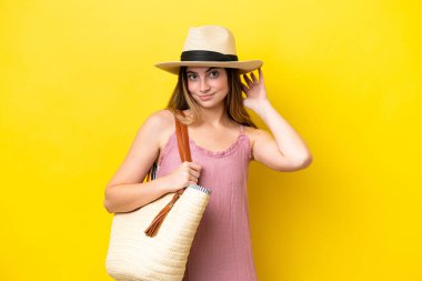 Young caucasian woman holding a beach bag isolated on yellow background having doubts