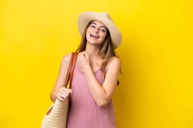 Young caucasian woman holding a beach bag isolated on yellow background celebrating a victory