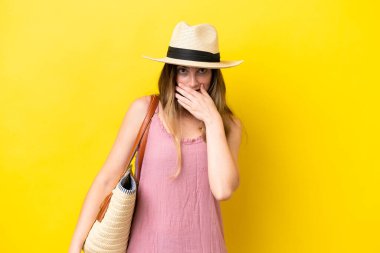 Young caucasian woman holding a beach bag isolated on yellow background happy and smiling covering mouth with hand