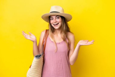 Young caucasian woman holding a beach bag isolated on yellow background with shocked facial expression