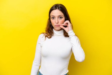 Sarı arka planda izole edilmiş genç beyaz kadın sessizlik işareti gösteriyor.