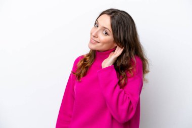 Beyaz arka planda izole edilmiş genç beyaz kadın elini kulağına koyarak bir şeyler dinliyor.