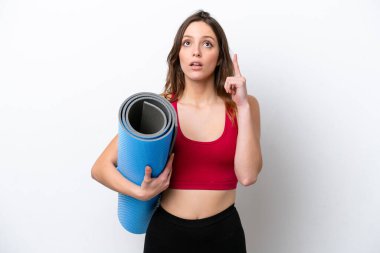 Beyaz arka planda izole edilmiş bir minderi tutarken yoga derslerine giden beyaz bir kadın parmağını yukarı kaldıran bir fikir düşünüyor.