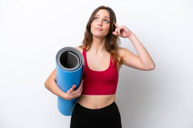 Beyaz arka planda izole edilmiş bir minderi tutarken yoga derslerine giden beyaz bir kadın şüpheleri ve düşünceleri var.