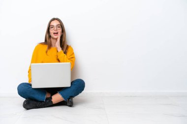 Yerde dizüstü bilgisayarlı beyaz bir kadın oturuyor beyaz arka planda izole bir şekilde ağzı açık bağırıyor.