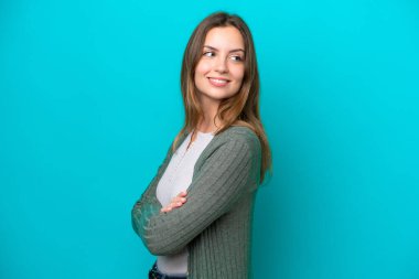 Mavi arka planda izole edilmiş, kolları bağlı ve mutlu genç beyaz bir kadın.