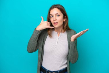 Kafkasyalı genç bir kadın mavi arka planda izole edilmiş telefon jestleri yapıyor.