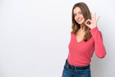 Beyaz arka planda izole edilmiş genç beyaz kadın parmaklarıyla tamam işareti gösteriyor.