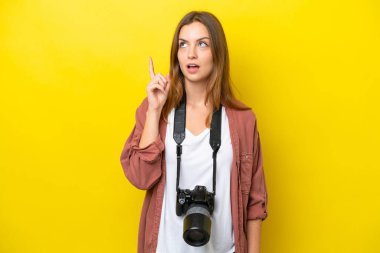 Genç fotoğrafçı beyaz kadın, sarı arka planda izole edilmiş.