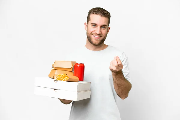 年轻英俊的金发男子举着比萨饼和汉堡包 在孤立的背景下做手势赚钱 — 图库照片