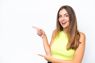 Beyaz arka planda izole edilmiş genç beyaz kadın şaşırmış ve işaret ediyor.