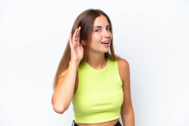 Beyaz arka planda izole edilmiş genç beyaz kadın elini kulağına koyarak bir şeyler dinliyor.