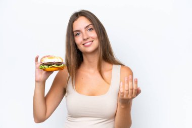 Beyaz arka planda izole edilmiş bir burger tutan genç ve güzel bir kadın, bizimle gelmesi için davet ediyor. Gelmene sevindim.