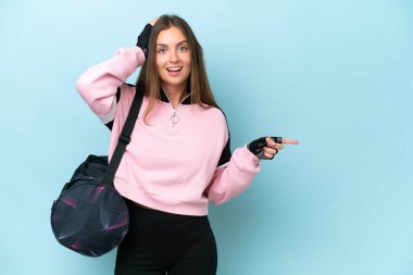 Young sport woman with sport bag isolated on blue background surprised and pointing finger to the side