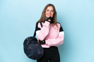 Young sport woman with sport bag isolated on blue background with glasses and smiling