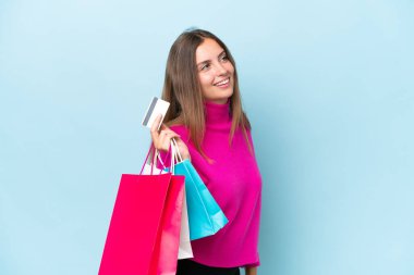 Mavi arka planda izole edilmiş genç bir kadın elinde alışveriş çantaları ve bir kredi kartı tutuyor.