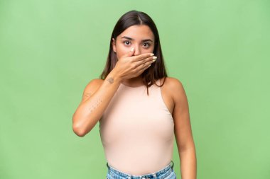 Young caucasian woman isolated on green chroma background covering mouth with hand