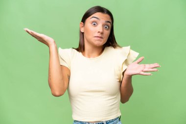 Young caucasian woman isolated on green chroma background making doubts gesture