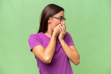 Young caucasian woman isolated on green chroma background covering mouth and looking to the side