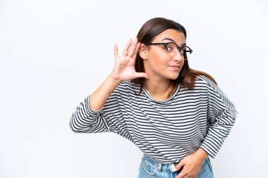 Beyaz arka planda izole edilmiş genç beyaz kadın elini kulağına koyarak bir şeyler dinliyor.