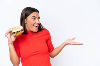 Beyaz arka planda yüzü sürpriz bir şekilde izole edilmiş hamburger tutan beyaz bir kadın.