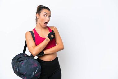 Young sport woman with sport bag isolated on white background surprised and pointing side