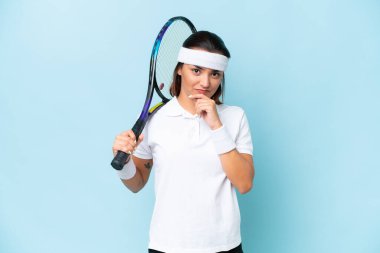 Genç tenisçi kadın mavi arka planda izole edilmiş düşünüyor.
