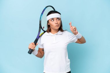 Genç tenisçi kadın mavi arka planda izole edilmiş parmakları çapraz ve en iyisini diliyor