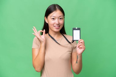 Young Asian woman with ID card over isolated background showing ok sign with fingers