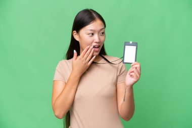 Young Asian woman with ID card over isolated background with surprise and shocked facial expression