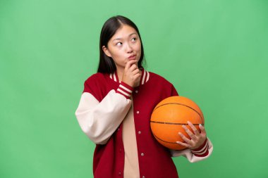 Young basketball player asian woman over isolated background and looking up