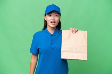 Young Asian woman taking a bag of takeaway food over isolated background with surprise facial expression