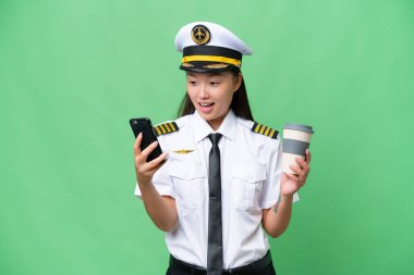 Airplane pilot Asian woman over isolated background holding coffee to take away and a mobile