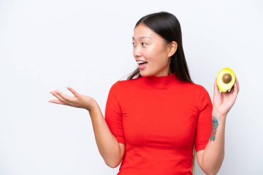 Young Asian woman holding an avocado isolated on white background with surprise facial expression