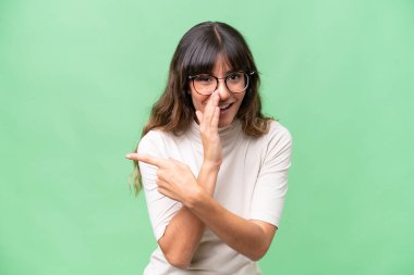 Tecrit edilmiş arka planda genç beyaz bir kadın bir ürünü sunmak ve bir şeyler fısıldamak için kenarı işaret ediyor.