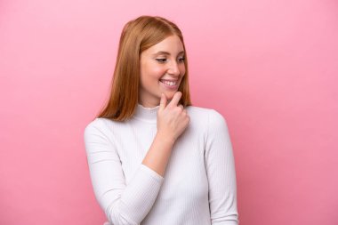 Genç kızıl saçlı kadın pembe arka planda izole edilmiş. Yan tarafa bakıyor ve gülümsüyor.