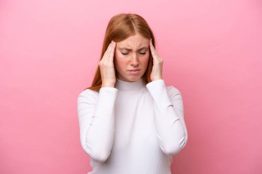 Pembe arka planda başağrısı olan genç, kızıl saçlı bir kadın.