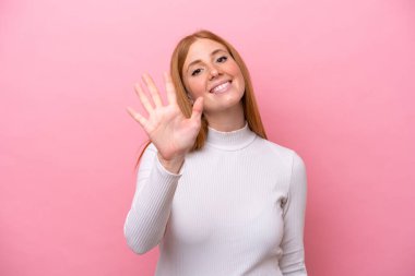 Pembe arka planda izole edilmiş genç kızıl saçlı kadın parmaklarıyla beşi sayıyor.