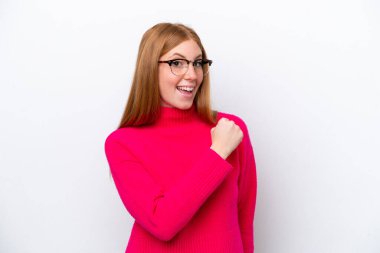 Genç kızıl saçlı kadın beyaz arka planda izole edilmiş zaferi kutluyor.