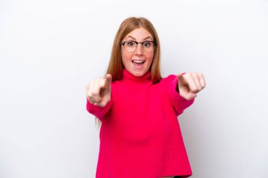 Beyaz arka planda izole edilmiş genç kızıl saçlı kadın şaşırmış ve ön tarafı işaret ediyor.