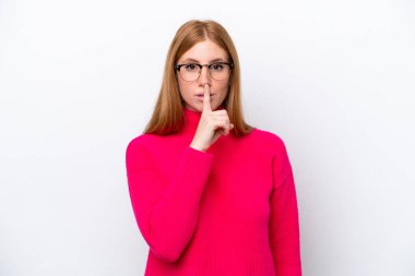 Beyaz arka planda izole edilmiş genç kızıl saçlı kadın sessiz bir jest işareti gösteriyor. Parmağını ağzına sokuyor.