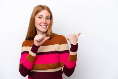 Beyaz arka planda izole edilmiş genç kızıl saçlı kadın bir ürünü sunmak için kenarı işaret ediyor.