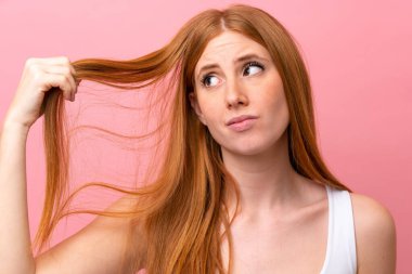 Genç kızıl saçlı kadın pembe arka planda izole edilmiş, saçları karışık. Portreyi kapat