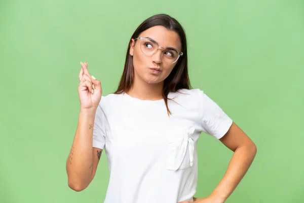 Young caucasian woman isolated on green chroma background with fingers crossing and wishing the best