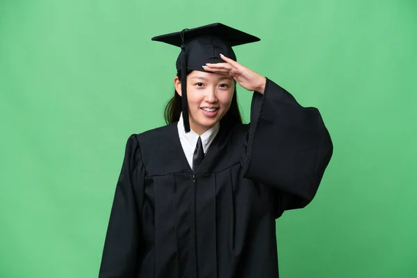 Young university graduate Asian woman over isolated background looking far away with hand to look something