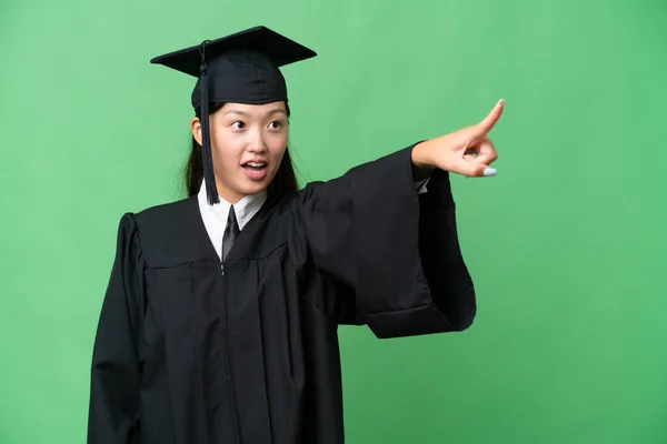 Young university graduate Asian woman over isolated background pointing away