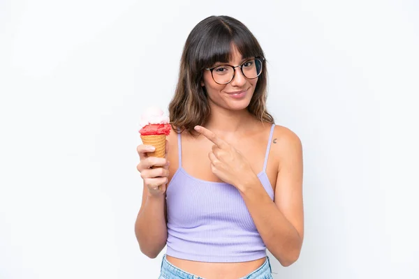Young caucasian woman with a cornet ice cream over isolated white background pointing to the side to present a product